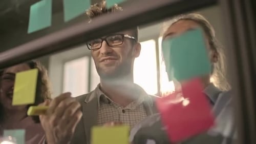 Creative Team Collaborating on Glass Wall with Sticky Notes