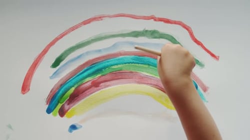 Child Painting a Colorful Rainbow on White Paper