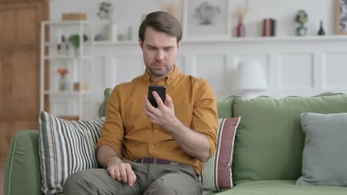 Man Reacts Negatively to Phone News on Couch