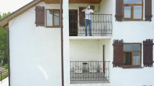 Man Drinking on Balcony of White Suburban House
