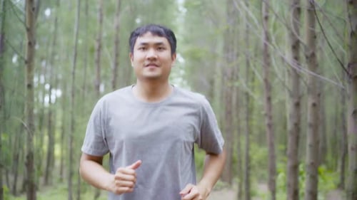 young athletic sporty Asian runner man in sports clothing running and jogging on forest trail.