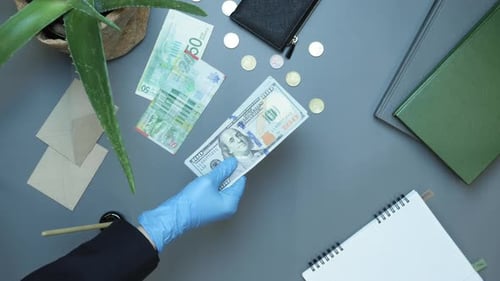 Gloves Handing Over Stack of Cash on Gray Desk