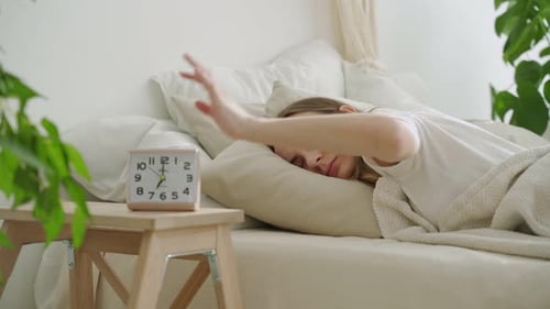 Young Woman Sleeping in Bed Turns Off Alarm