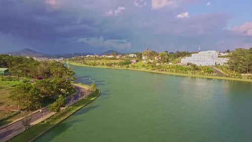 Flycam Moves Over Wide Lake Road and City on Banks