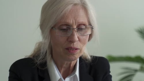 An Elderly Businesswoman Works at a Laptop Takes Off Her Glasses Thinks and Looks Out the Window