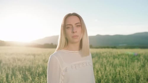 Attractive Caucasian girl posing in front of camera in rural farm field with sunset in background.