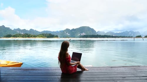 Woman Freelancer Sitting on Wooden Pier on Lake and Work on Project on Laptop