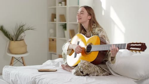 Woman Plays Guitar and Sings on Bed