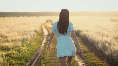 Woman in Beautiful Waving Dress Walks on the Meadow Happy Summer Vacation Sky at Sunset
