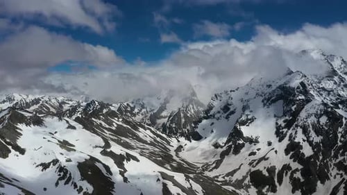 Air Flight Through Mountain Clouds Over Beautiful Snowcapped Peaks of Mountains and Glaciers