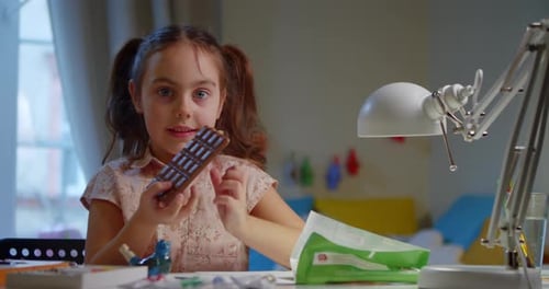 Happy Smiling Girl Bites Delicious Chocolate While Sitting Table in the Room