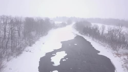 Luftaufnahme, die während eines Schneesturms über einen halb gefrorenen Fluss fliegt