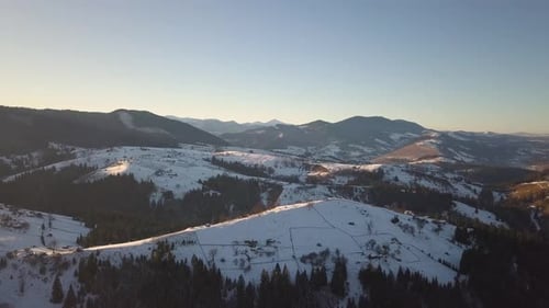 Aerial view of small village with scattered houses on snow covered hills in winter and bare dark