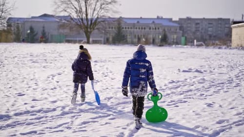 Frost winter season. Two children walk a winter road with plastic spade sledges.