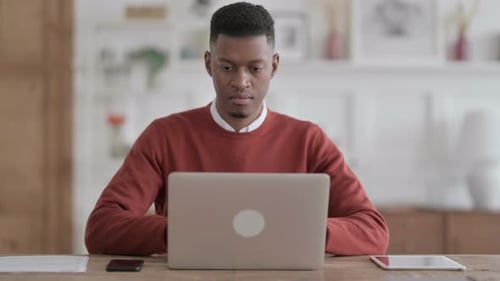 African Man Looking at Camera while using Laptop in Office