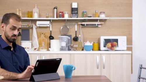 Man Using Tablet in Kitchen With Coffee