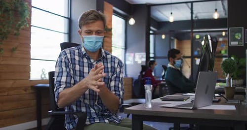 Caucasian man wearing face mask using hand sanitizing at modern office
