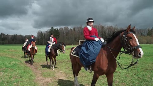 Damen in leuchtenden mittelalterlichen Kostümen reiten auf einem Pferd durch ein Feld Rekonstruktion Mittelalterliche Frauen