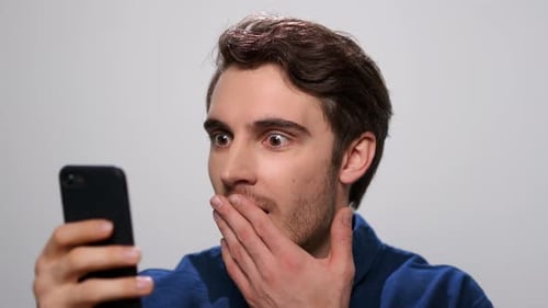 Shocked Man Reading News on Smartphone in Studio. Guy Using Mobile Phone