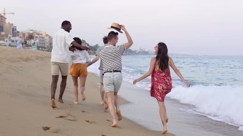 Happy Friends Barefoot Running Together Along the Beach at Sunset Splashing in the Water Waves