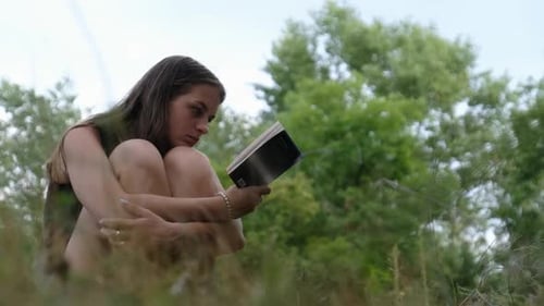 Young Woman Reading Book in a Grassy Field