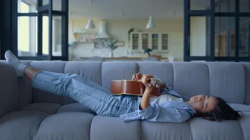 Woman Plays Guitar Lying on Couch at Home