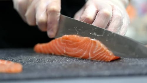 Hands Cutting Salmon with Knife on Cutting Board