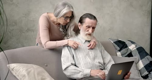 Elderly Couple Using Laptop Together on Sofa at Home