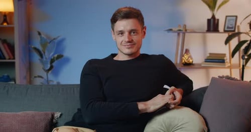 Portrait of Cheerful Young Man Turning Head To Camera Whole Sitting on Sofa. Front View of Handsome