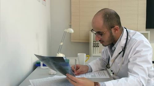 Concentrated Young Male Doctor Examining Xray Image and Filling in Form