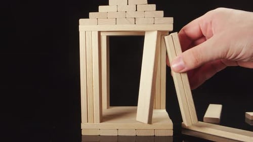 Human Hand Repairs A Wooden House On A Black Background