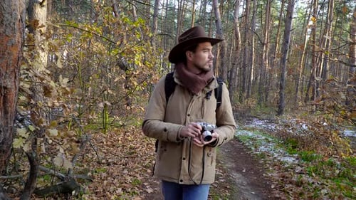 Backpacker with Camera Walks Along a Trail in the Forest