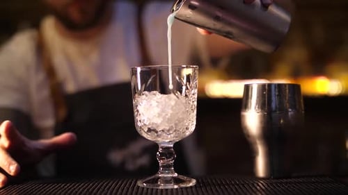 Bartender Pouring Cocktail into Glass Filled with Ice