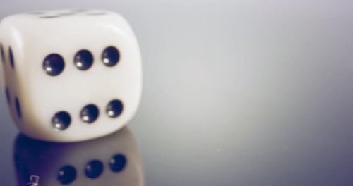 Macro disparo a cámara lenta de dados blancos cayendo y rodando sobre una superficie reflectante