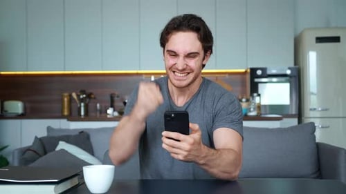 Excited Man Celebrating Success While Looking at Phone