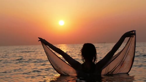 Woman in Ocean Holding Sheer Fabric at Sunset
