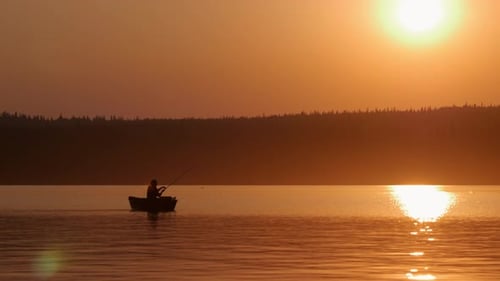 Mann sitzt in einem Boot auf dem Fluss und fischt am wunderschönen orangefarbenen Sonnenuntergang