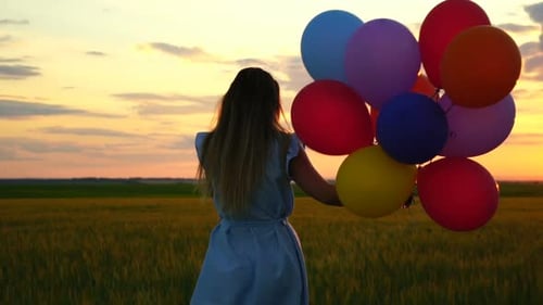 Happy Woman with Balloons Running in the Wheat Field at Sunset