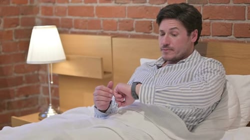 Middle Aged Man Checking Watch while Waiting in Bed