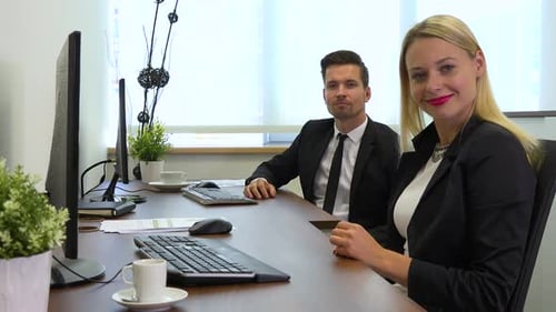 Two Office Workers, Man and Woman, Work on Computers and Nod at The Camera with A Smile