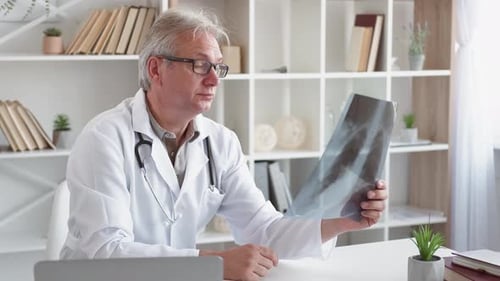 Doctor Examining X-Ray Looking Fatigued in Office