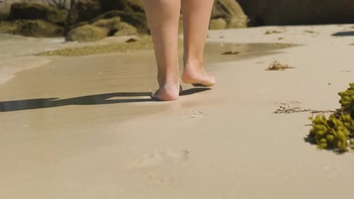 A close up shot of the heels of a young female walking leisurely across a beach, shallow ocean waves