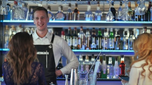 Bartender Serving Customers at a Modern, Lit Bar