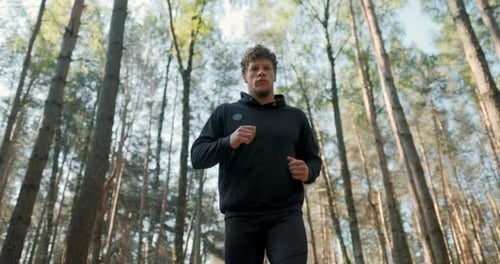 Slow Motion Shot of Man Running Through Pine Forest on Path in Woods. Runner Training Fitness and