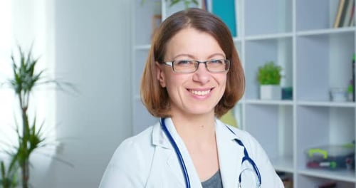 Portrait of a smiling woman doctor sitting in the interior of the office. 4K