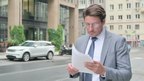 Businessman Reading Documents on City Street