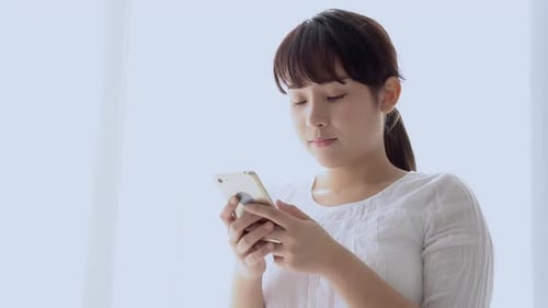 Junge asiatische Frau lächelt und schaut auf ihr Smartphone und liest das soziale Netzwerk mit Vergnügen.