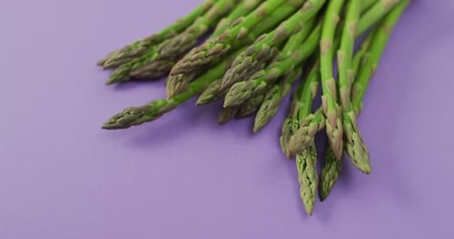 Video of close up of fresh asparagus with copy space over lilac background