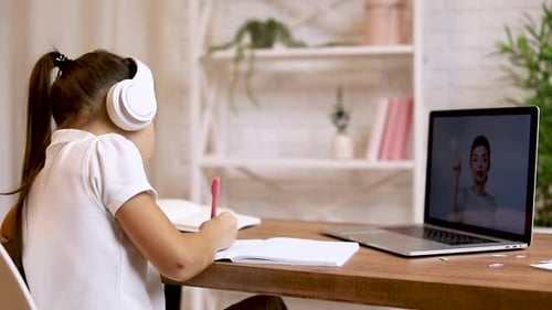 Girl Writing at Desk with Laptop and Headphones