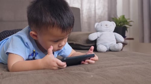 Little Boy Uses Smartphone on Couch at Home